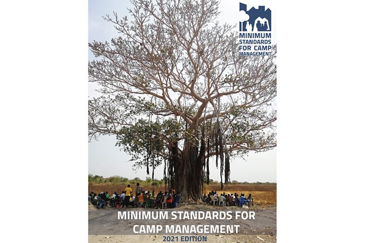 An image of the front cover of the “Minimum standards for camp management” handbook (2021 edition), featuring a photo of a very large tree with with a horde of people gathered under it.