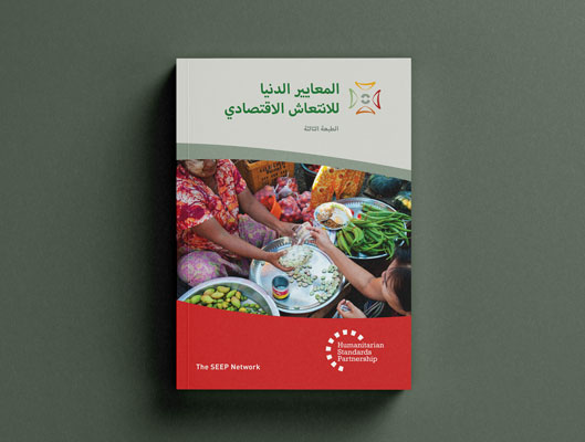 A photo-realistic mock-up of a printed Arabic “Minimum Economic Recovery Standards (MERS)” handbook, including the title and a photo of a market stall where a woman is trading some cash for a bag of beans.